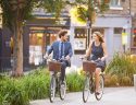 Businesswoman And Businessman Riding Bike Through City Park