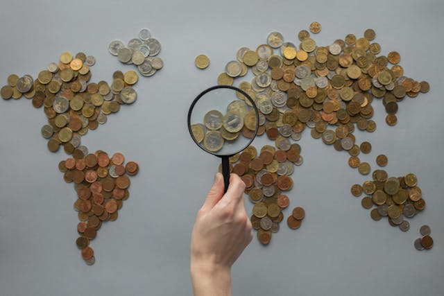 anonymous-person-with-magnifying-glass-over-world-map-of-coins